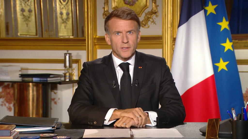Emmanuel Macron sentado ante un escritorio, con las banderas francesa y europea a su lado.