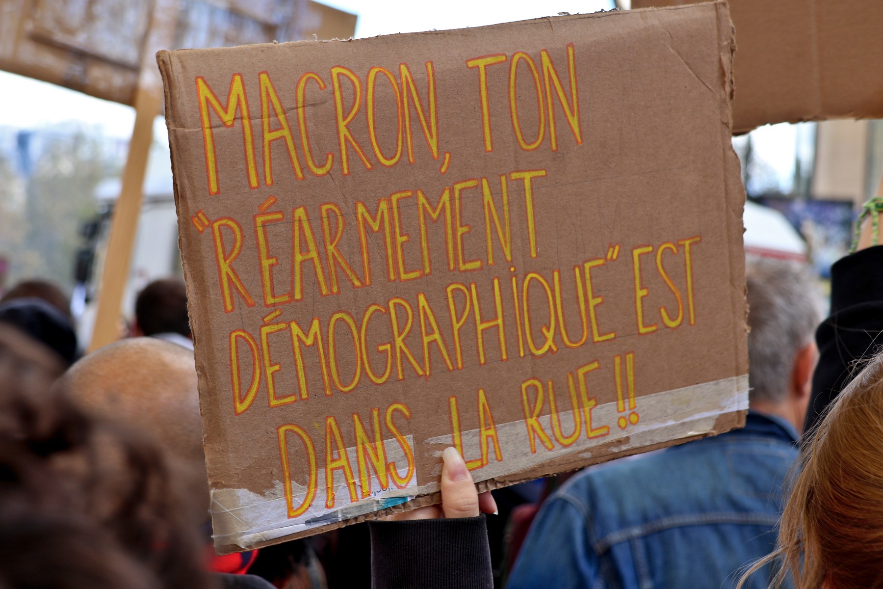 Una persona sostiene una pancarta dirigida a Macron entre los asistentes a la manifestación de París del 17 de octubre de 2026.